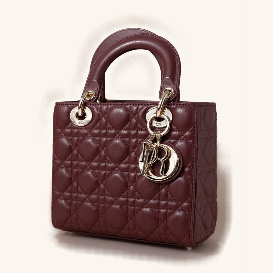 Bolsa bordô estruturada em couro acolchoado, duas alças curtas no topo e pingentes de metal na lateral.